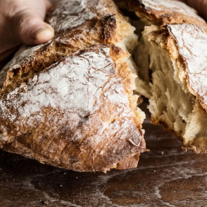 Hands tearing crusty rustic loaf of bread