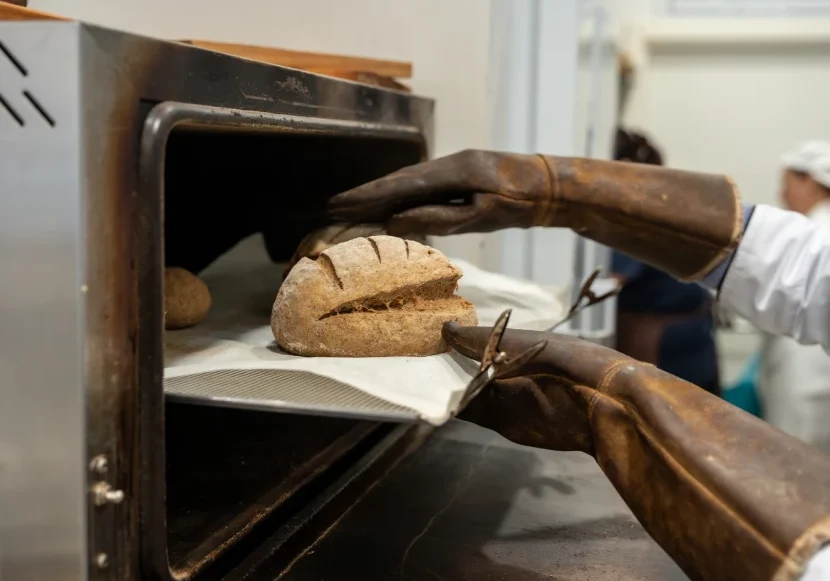Gloved hands removing sourdough loaf from oven