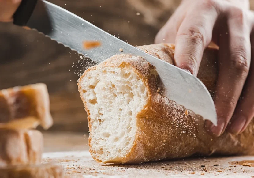 Hands slicing fresh crusty baguette with serrated knife