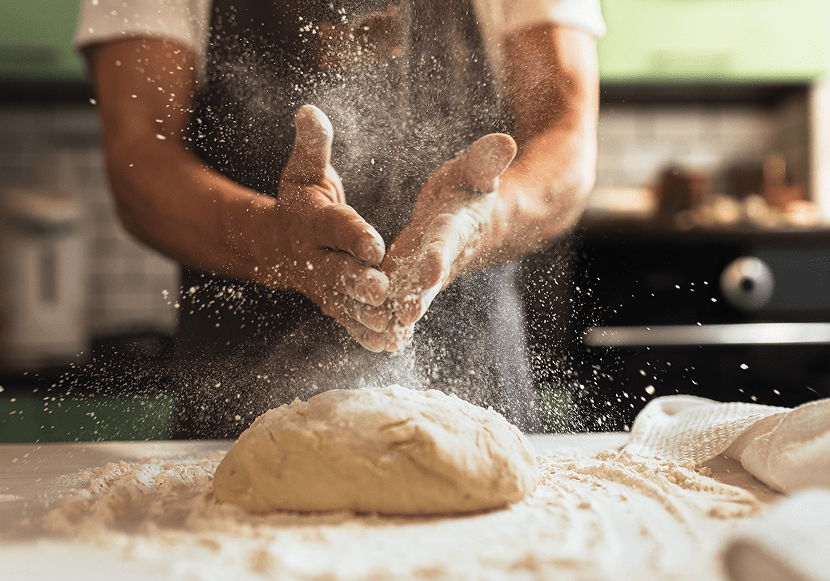 Baker's hands dusting flour over bread dough